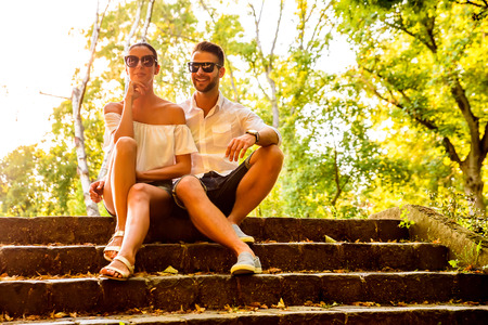 A beautiful young couple sitting on the stairs in a park in the sunsetの写真素材
