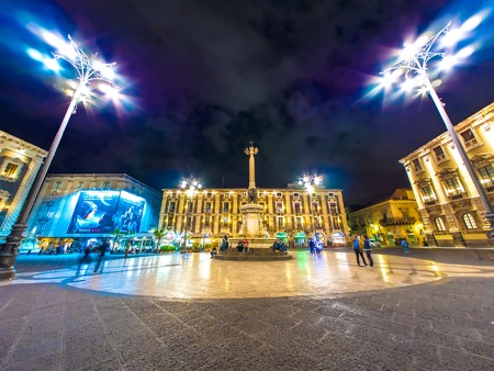 CATANIA, ITALY - CIRCA JUNE 2018: View on historic architecture of the main square as people pass by on the cobblestones streets at night circa June 2018 in Catania, Italy.のeditorial素材