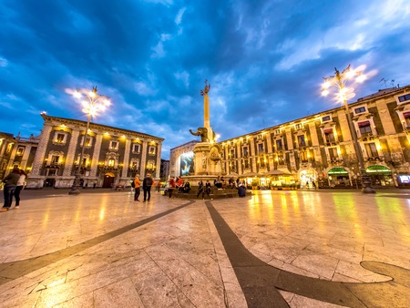 CATANIA, ITALY - CIRCA JUNE 2018: View on historic architecture of the main square as people pass by on the cobblestones streets during dusk circa June 2018 in Catania, Italy.のeditorial素材
