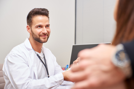 A handsome male doctor shows ultrasound picture to the young pregnant couple.の写真素材