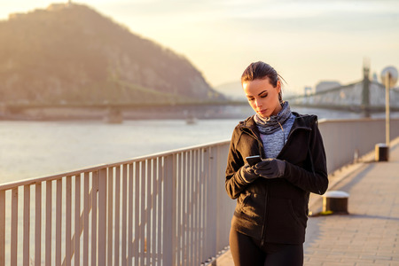 Young sporty woman standing in the sunset with a mobile