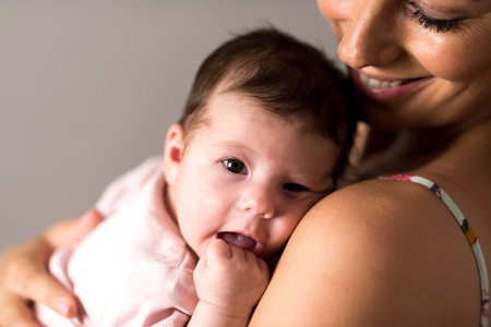Closeup photo of a baby while her mother holding her on her chest while standing in front of a grey background in a studio.の写真素材