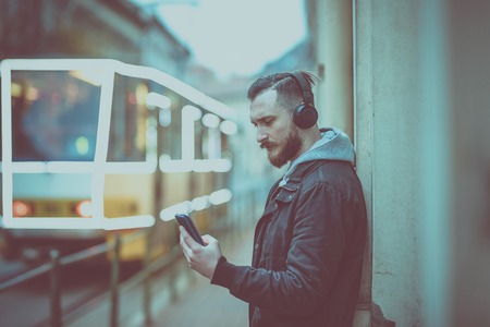 A retro style photo of a hipster man while checking his smartphone in an urban environment.