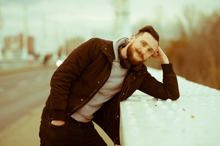 A retro style photo of a thinking handsome young hipster man while leaning on the bridges railing.