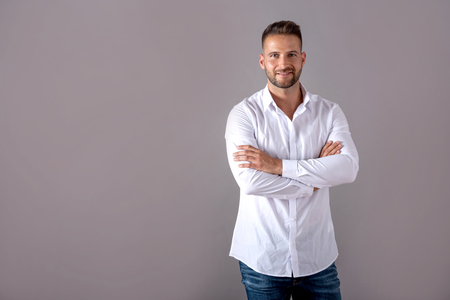 A smiling handsome young man in a white shirt standing in front of a grey background in the studio.の写真素材