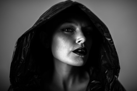 Emotive photo of a beautiful bald woman in a black raincoat with the hoods on.の写真素材