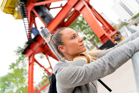 An athletic woman in a grey sweater resting and leaning on the bridge railing with headphones around...
