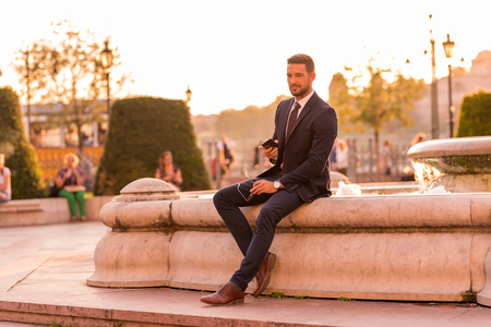 A handsome young businessman sitting next to a fountain on a sunny day.の写真素材