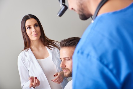 A beautiful assistant and a handsome doctor consulting over patient in the hospital room.の写真素材