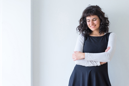 Portrait of a beautiful smiling young woman in an elegant dress while standing in front of a white wall.の写真素材