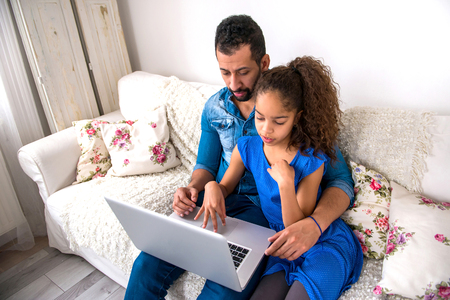 Black father and his daughter siting on a couch with a laptop