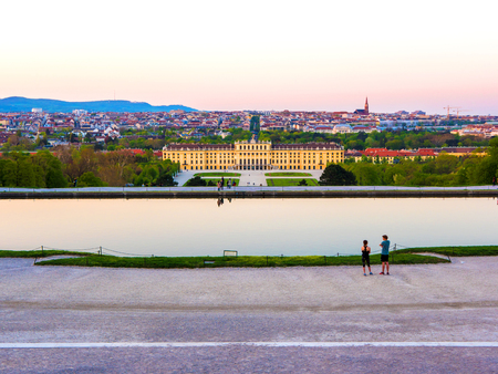 VIENNA, AUSTRIA - CIRCA APRIL 2018: Panorama view on the baroque architecture of the Schoenbrunn Palace as tourist pass by at the lake and on the walkway of the castle park circa April 2018 in Vienna, Austria.のeditorial素材