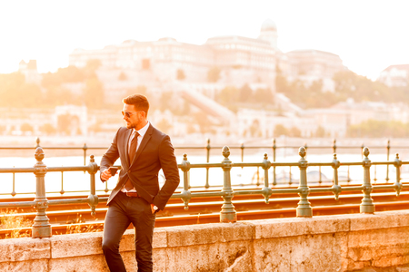A handsome young businessman standing and waiting next to a tramline on a sunny day.の写真素材