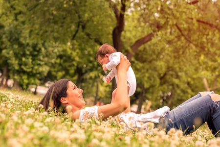 A young mother lying on the grass in the park while holding her baby in her arms.の写真素材