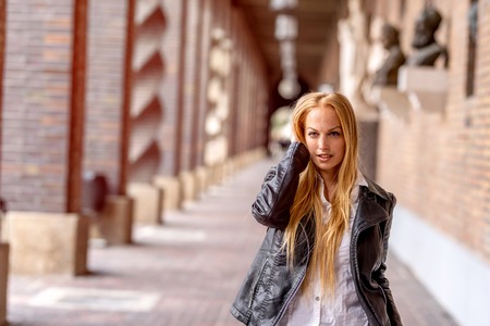 A beautiful woman in a leather jacket walking on the alley of a historic European building.の写真素材
