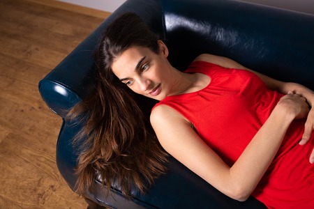 A beautiful smiling young woman in a red dress lying on a sofa.