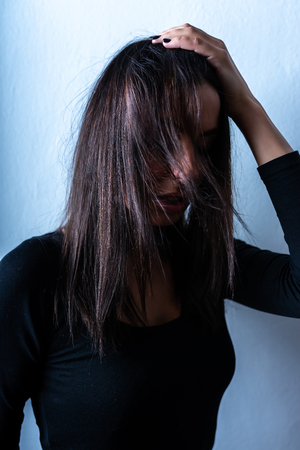 Dark mood sensual portrait of a beautiful woman while leaning against a white wall.の写真素材