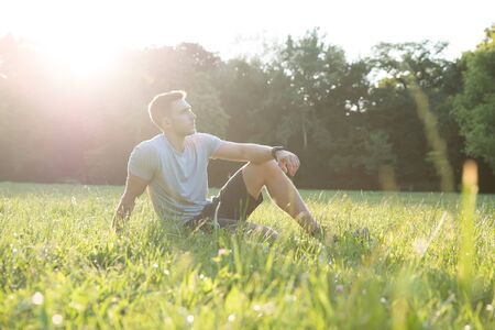 A handsome young man relaxing in the sunset and sitting in the grass.の写真素材