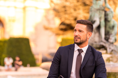 A handsome young businessman sitting next to a fountain on a sunny day.の写真素材