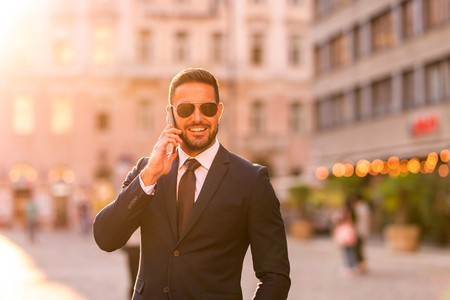 A handsome young businessman walking on the streets and talking on his phone on a sunny day.の写真素材