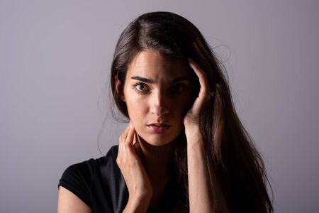 Sensual photo of a beautiful serious young woman in an elegant black dress sitting on a sofa.