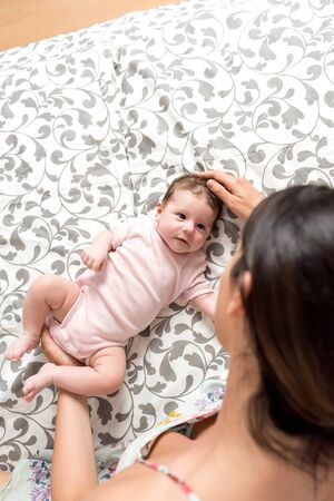 A young mother and her baby girl lying on a patterned grey blanket.