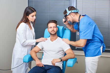 A handsome doctor with a beautiful assistant examining the patient in the hospital room.
