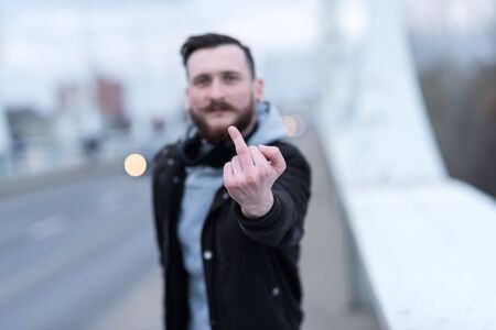 A handsome young hipster man showing his middle finger to the camera in an urban environment.