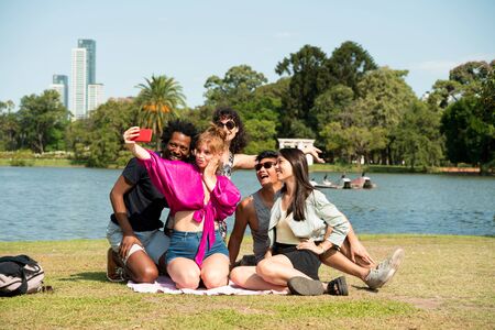 A divers group of friends taking selfies while sitting at a lake on a sunny day.の写真素材