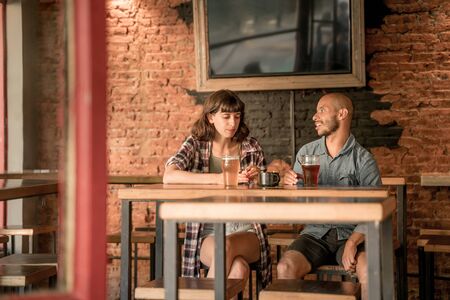 A young couple sitting at a table in a bar, pub or restaurant while having fun and drinking beer.の写真素材