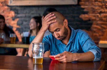 A sad lonely latin man sitting in a bar or pub while drinking beer.