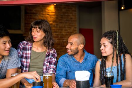 A group of friends conversating and sitting together in a bar or pub while having beer.の写真素材
