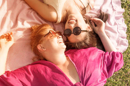 Two young female friends laying together in the grass on a hot summer day.