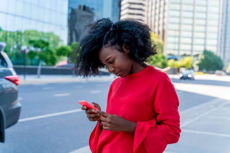 A beautiful black woman using her phone in a big city.