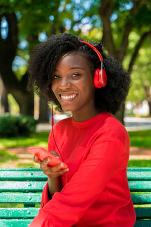 A young black woman listening to music on her headphones in a park.の写真素材