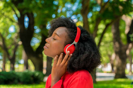 A young black woman listening to music on her headphones in a park.の写真素材