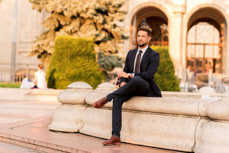 A handsome young businessman sitting next to a fountain on a sunny day.の写真素材