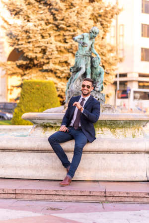 A handsome young businessman sitting next to a fountain on a sunny day.の写真素材