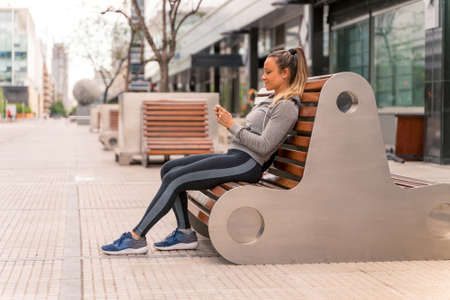 An athletic woman sitting on a bench and using her smartphone