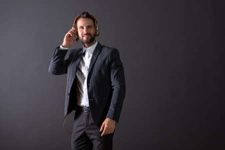A smiling handsome young businessman in a suit listening to music in front of a dark grey background...
