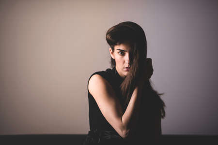 Sensual photo of a beautiful serious young woman in an elegant black dress sitting on a sofa.の写真素材
