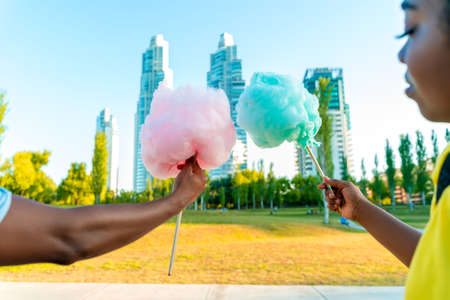 A happy black couple having colourful candy floss together in a park of a big city.の写真素材