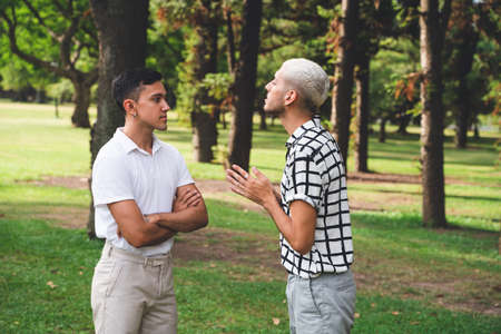 Annoyed latin american gay couple having relationship problem standing in a parkの写真素材