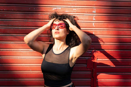 Portrait of a young woman wearing red sunglasses grabbing her hair.