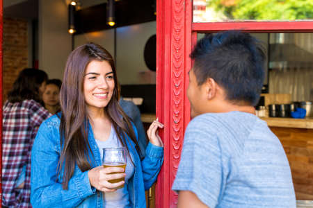 A handsome asian man flirting with a latin woman at the entry of a bar while having drinks.の写真素材