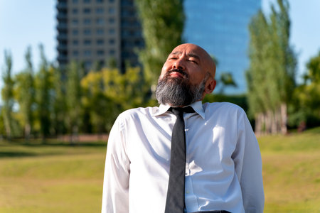Asian businessman enjoying sunshine sitting in a park in a metropolis at break time.の写真素材