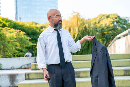 Formal dressed Asian businessman standing on the stairs in a park in a metropolis.