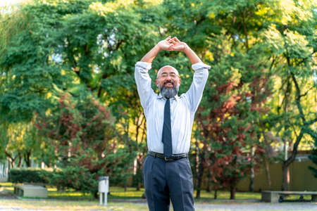 Asian businessman having a break and stretching in a park in an urban environment.の写真素材