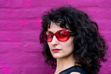 Young woman portrait wearing red sunglasses at a pink brick wall