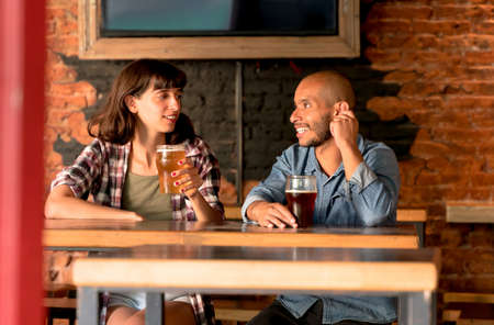 A young couple sitting at a table in a bar, pub or restaurant while having fun and drinking beer.の写真素材